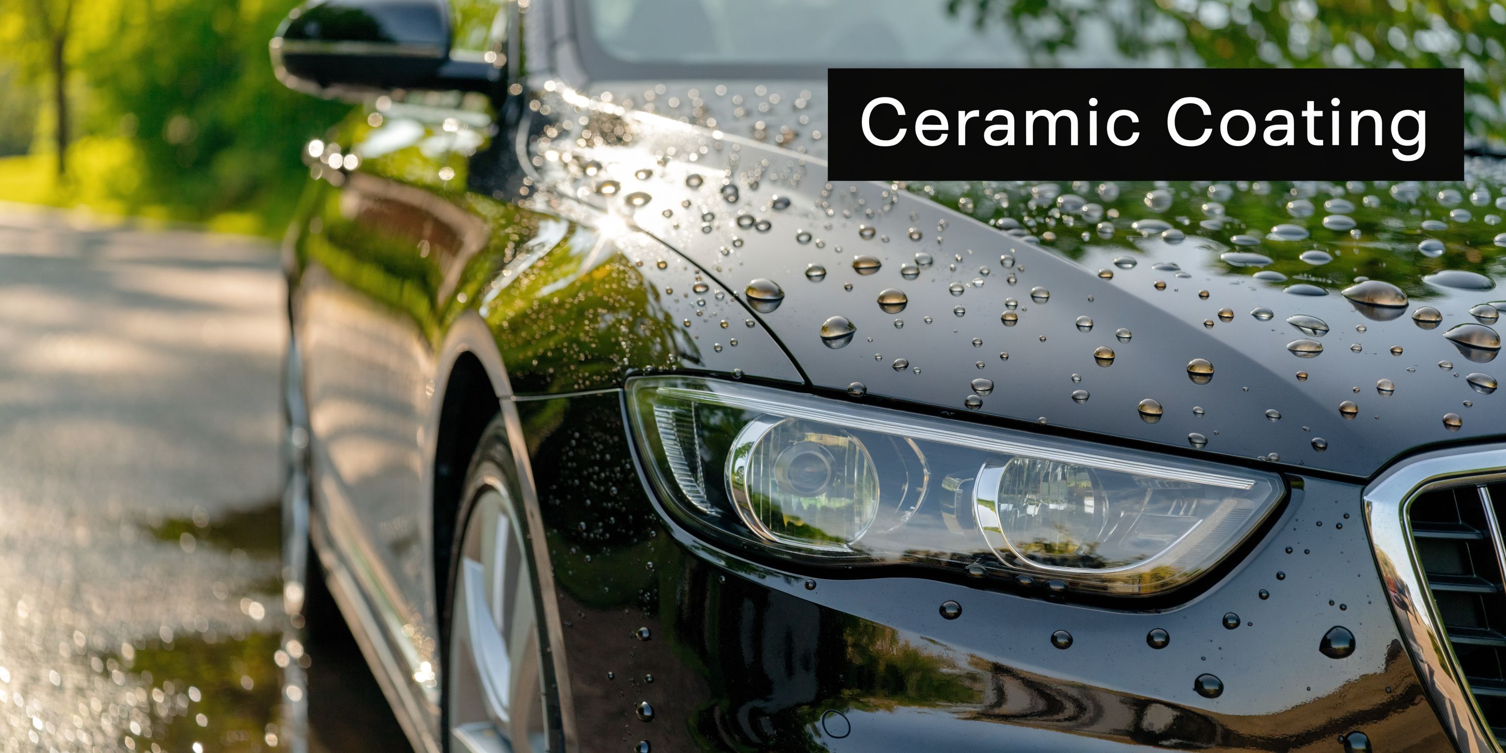 A close-up view of a shiny black car with water beads on its hood, demonstrating ceramic coating benefits.