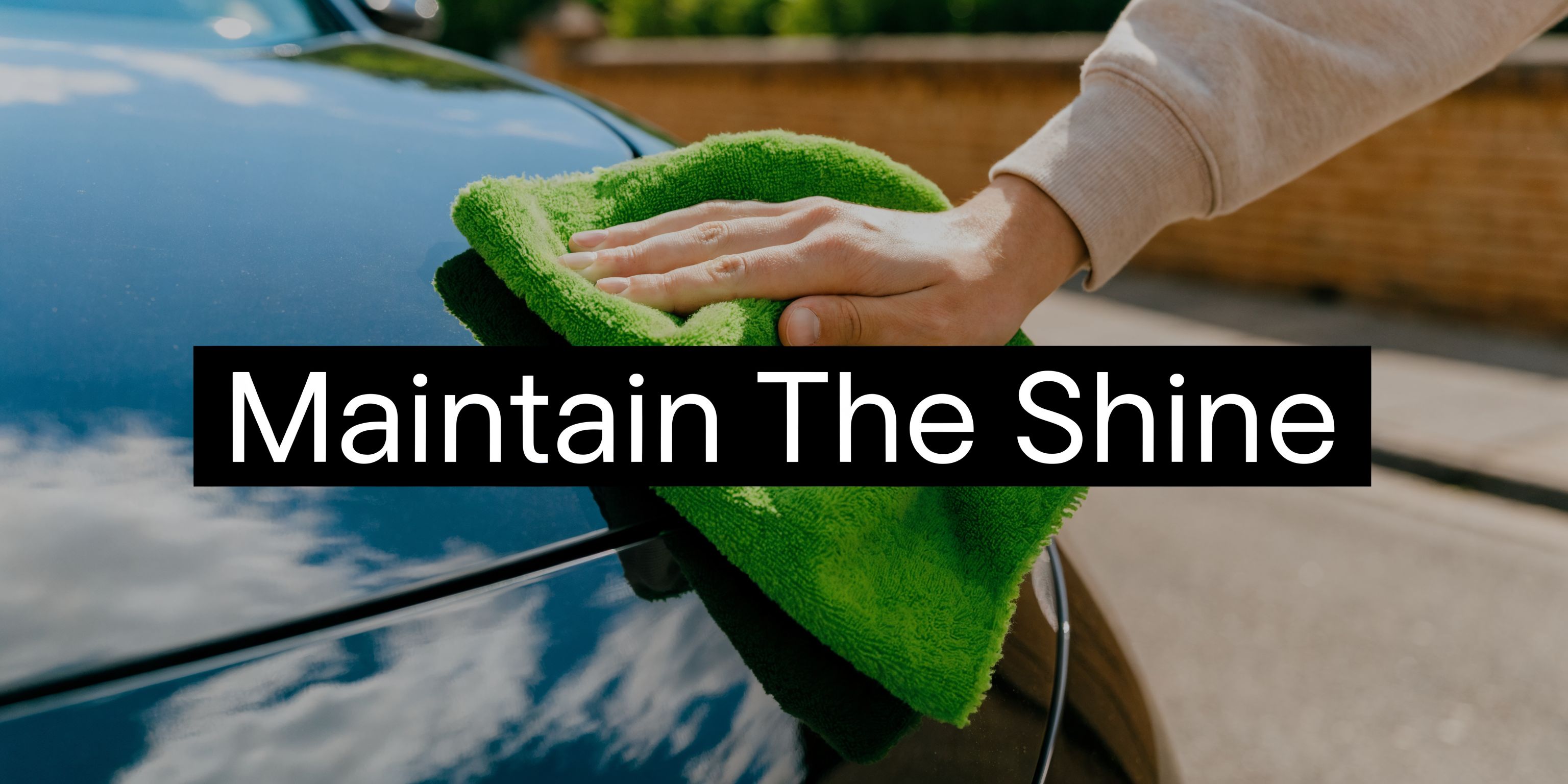 A close-up shot of a hand using a green microfiber cloth to wipe a shiny black car.